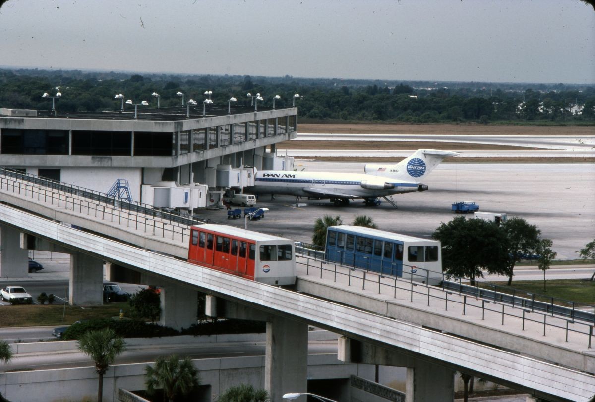 Original first-generation Westinghouse C-100 shuttles on their guideways at Tampa International Airport in 1982, with a Pan Am jet parked behind.
