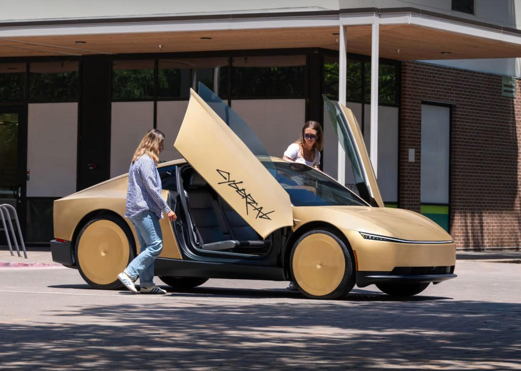 Passengers boarding a gold Tesla Cybercab with gull-wing doors open, exposing the two-seat cabin.
