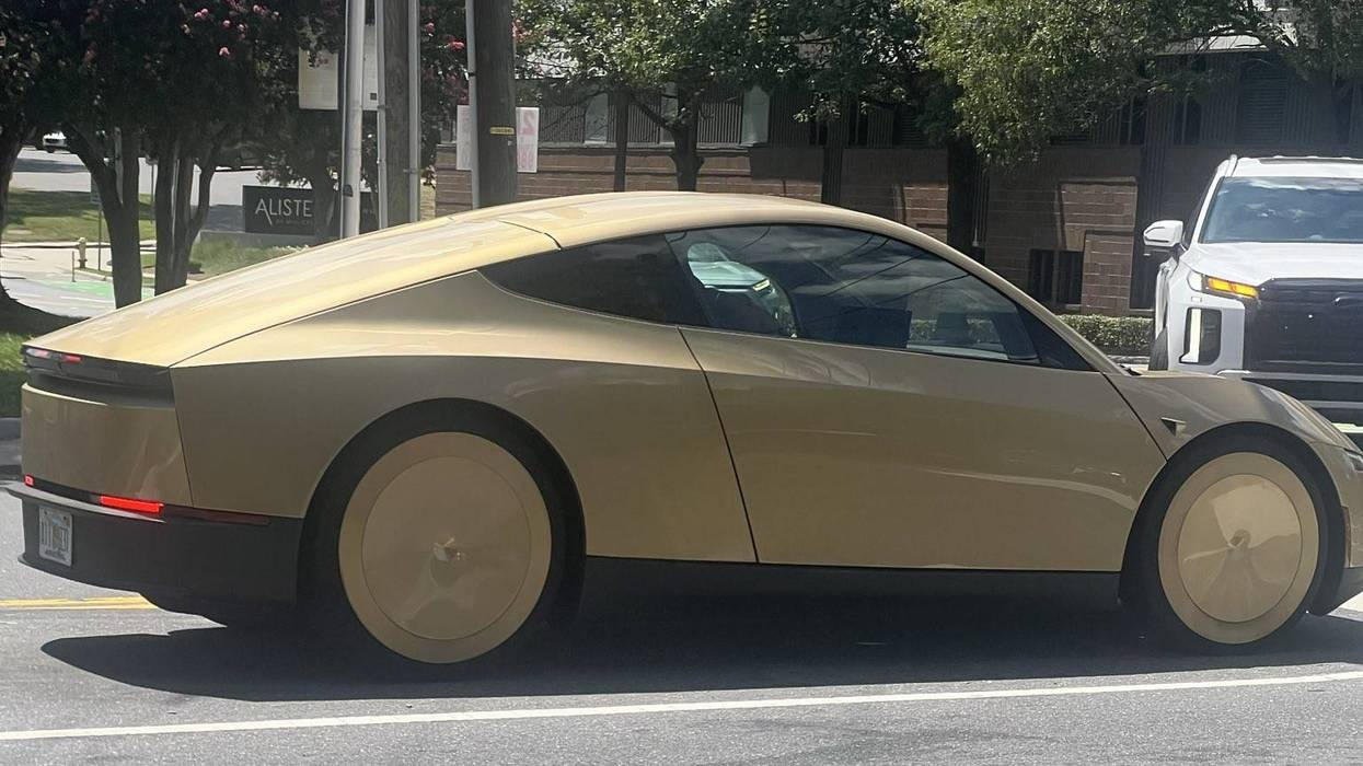 A gold Tesla Cybercab in profile on a city street, with no side mirrors or conventional driver controls.