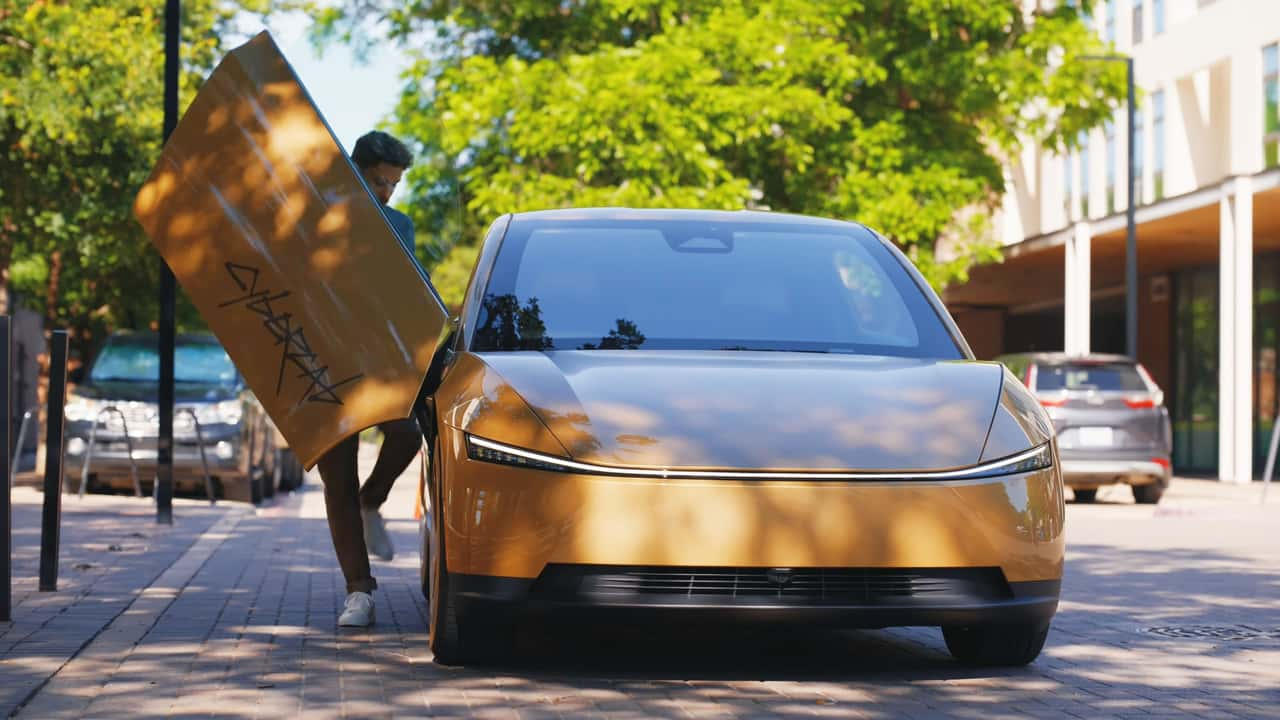 Front view of a gold Tesla Cybercab with a gull-wing door open and no conventional grille or side mirrors.