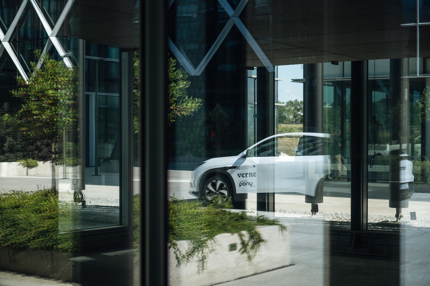 A Verne robotaxi marked with Pony.ai branding, seen reflected in the glass of a building in Zagreb.