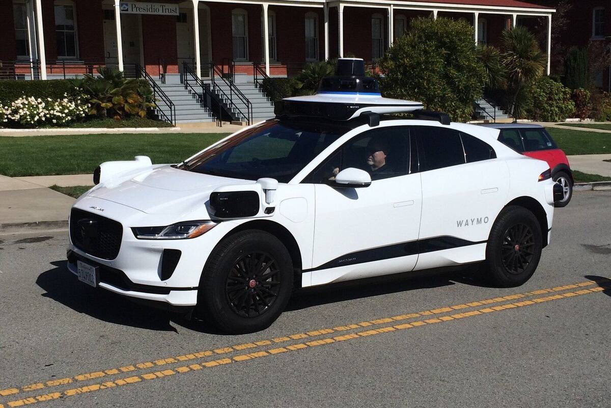 A white Waymo Jaguar I-PACE with a roof sensor suite parked on a street.