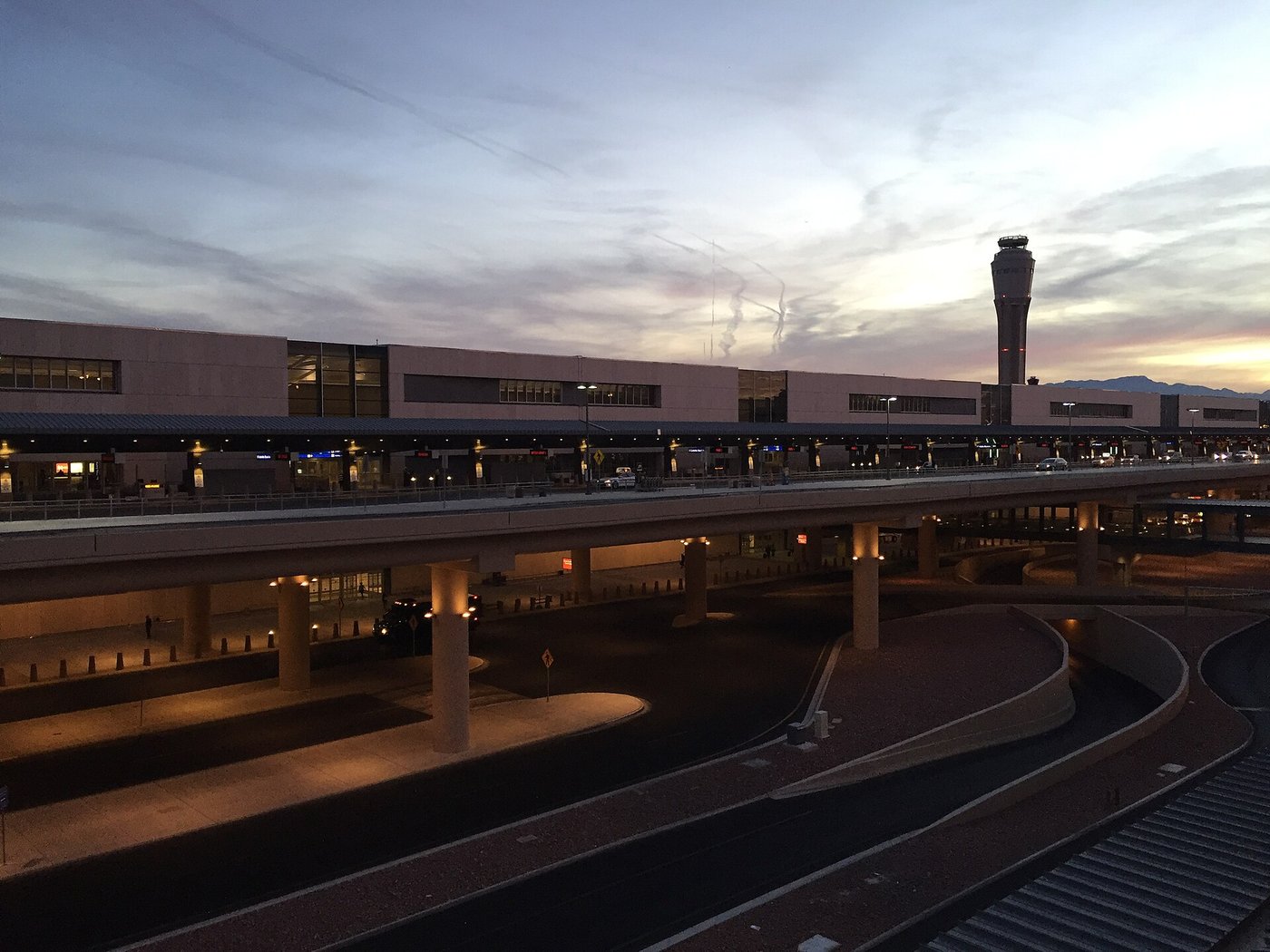 The curbside roadways outside Terminal 3 at Harry Reid International Airport, then McCarran International Airport, at dusk, with the control tower in the background.