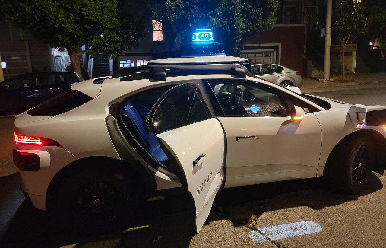 A Waymo Jaguar I-PACE at night, illustrative U.S. street scene.