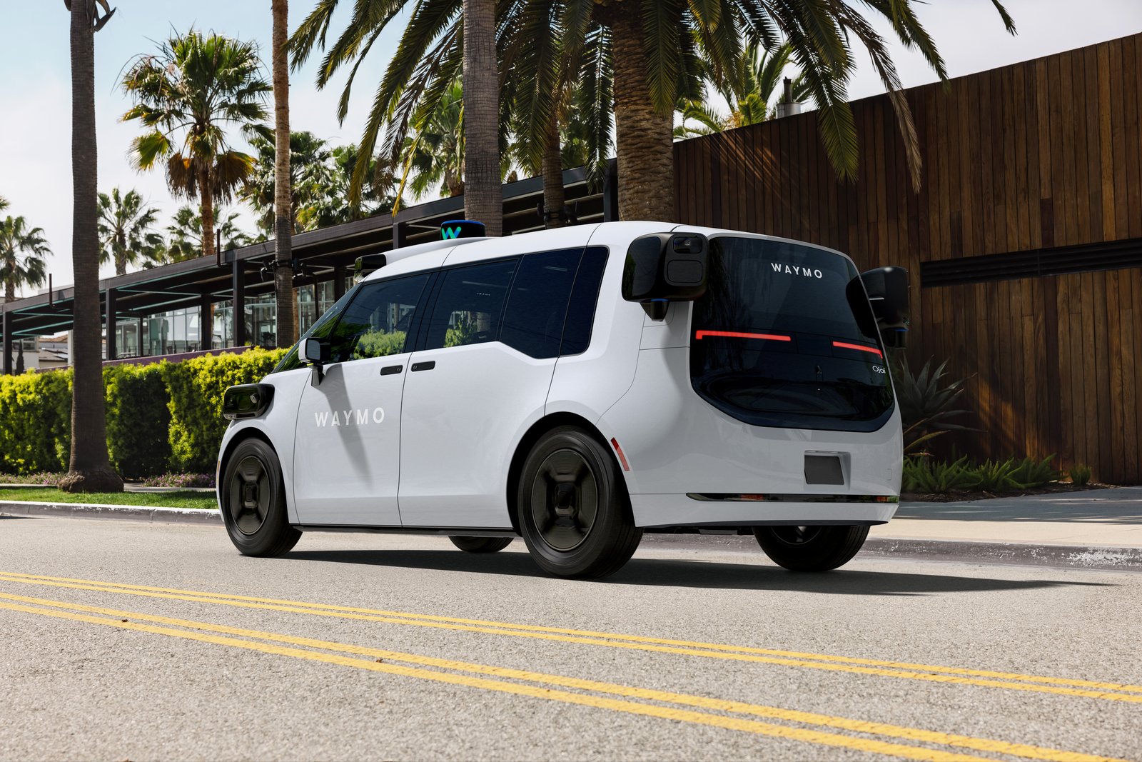 Rear three-quarter view of a Waymo Ojai robotaxi on a Las Vegas street, empty front seat.