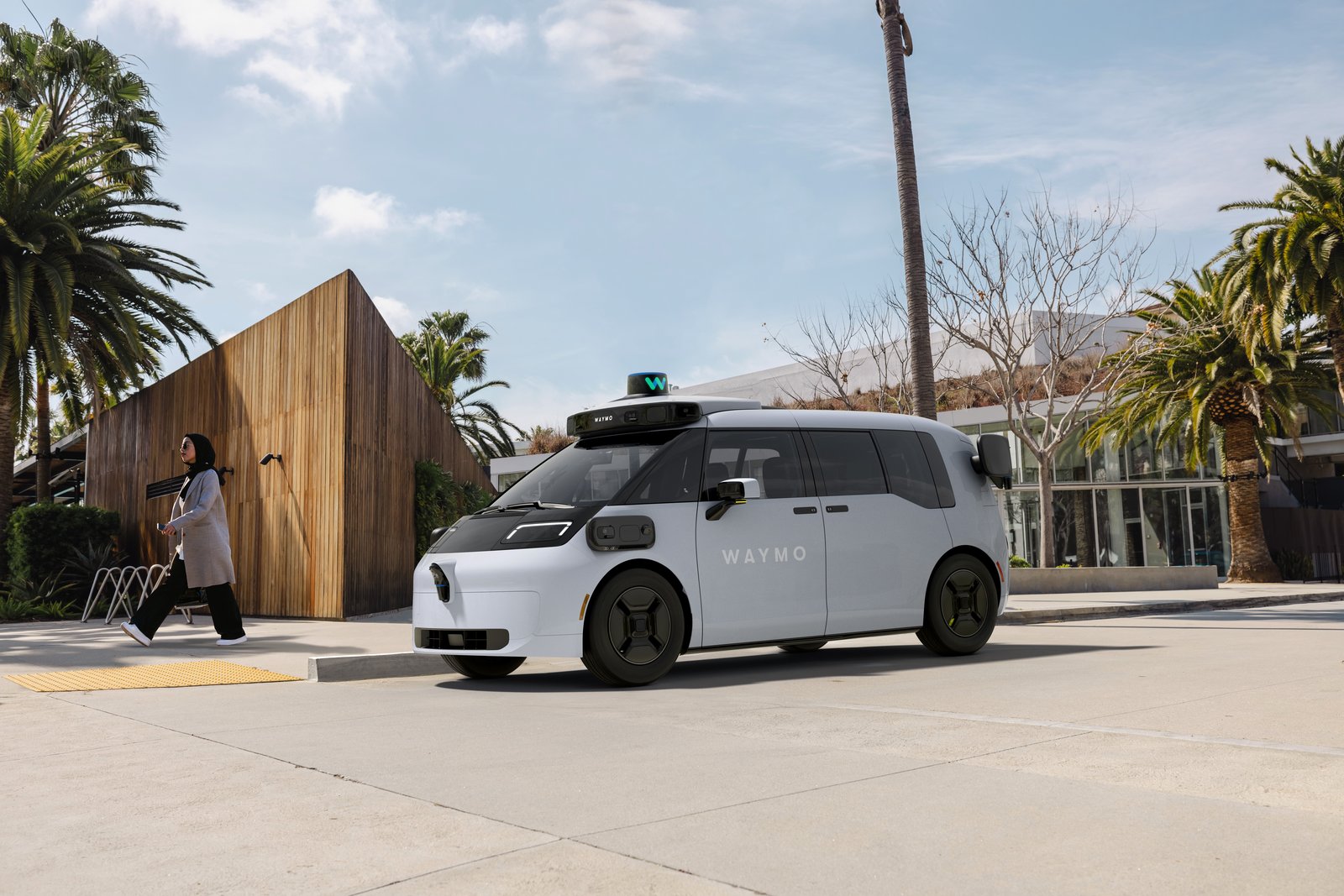 A Waymo Ojai robotaxi at a curb in Las Vegas, with a pedestrian walking nearby.